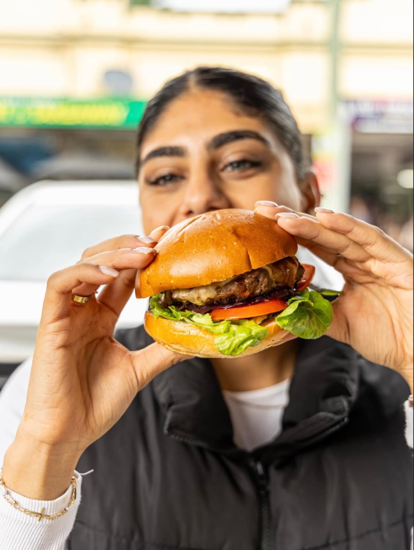 A customer holding a burger with both hands outside the shopfront