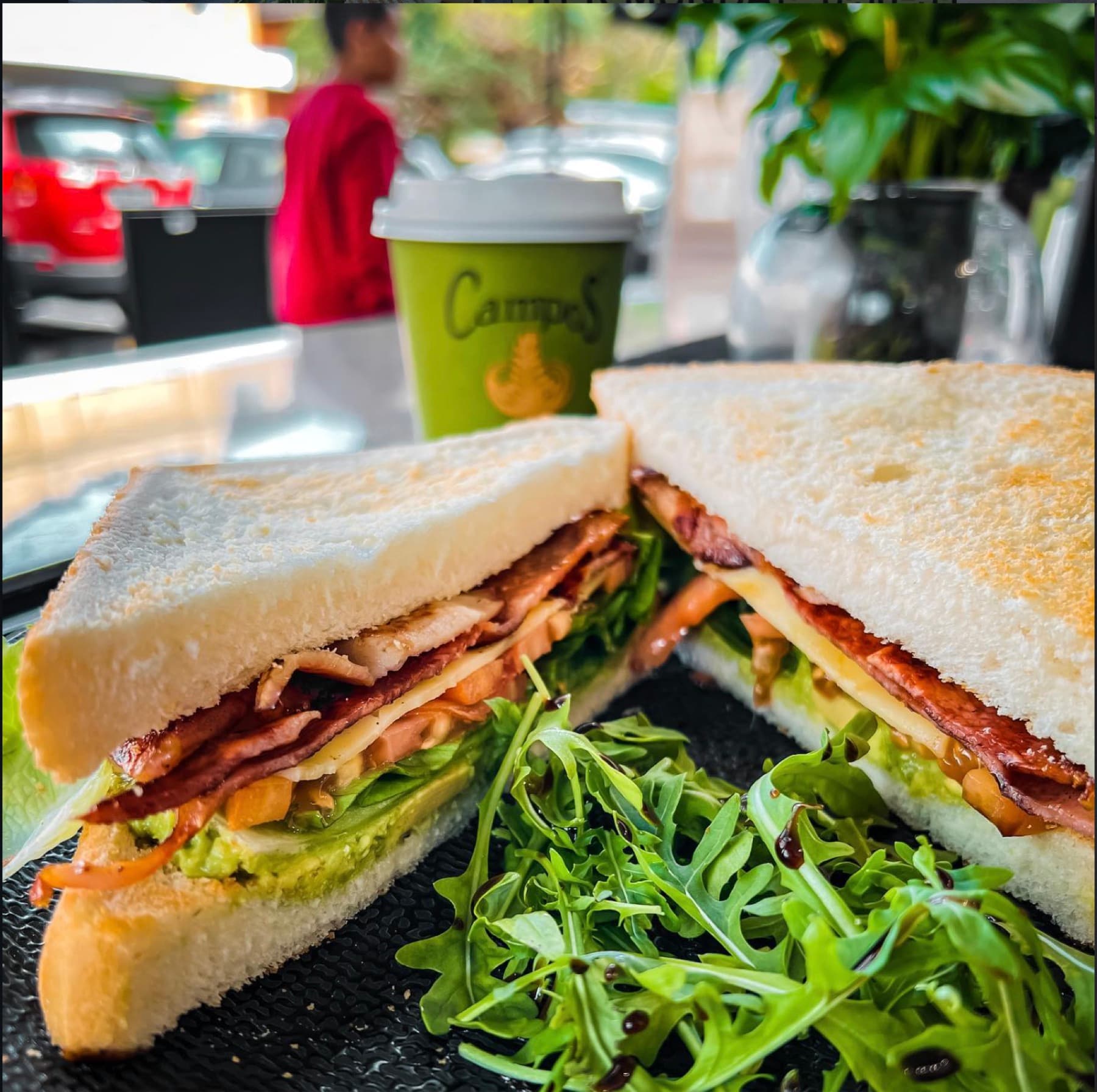 A club sandwich on white bread with bacon, cheese and avocado, served with rocket