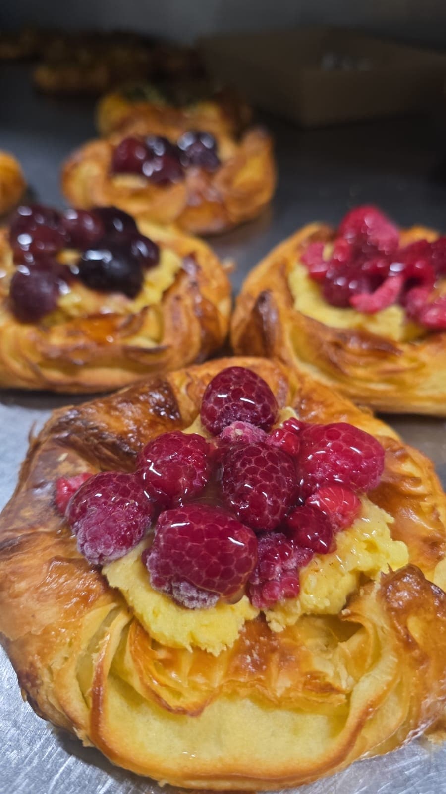 Raspberry and custard danishes cooling on a bench, glazed and still warm