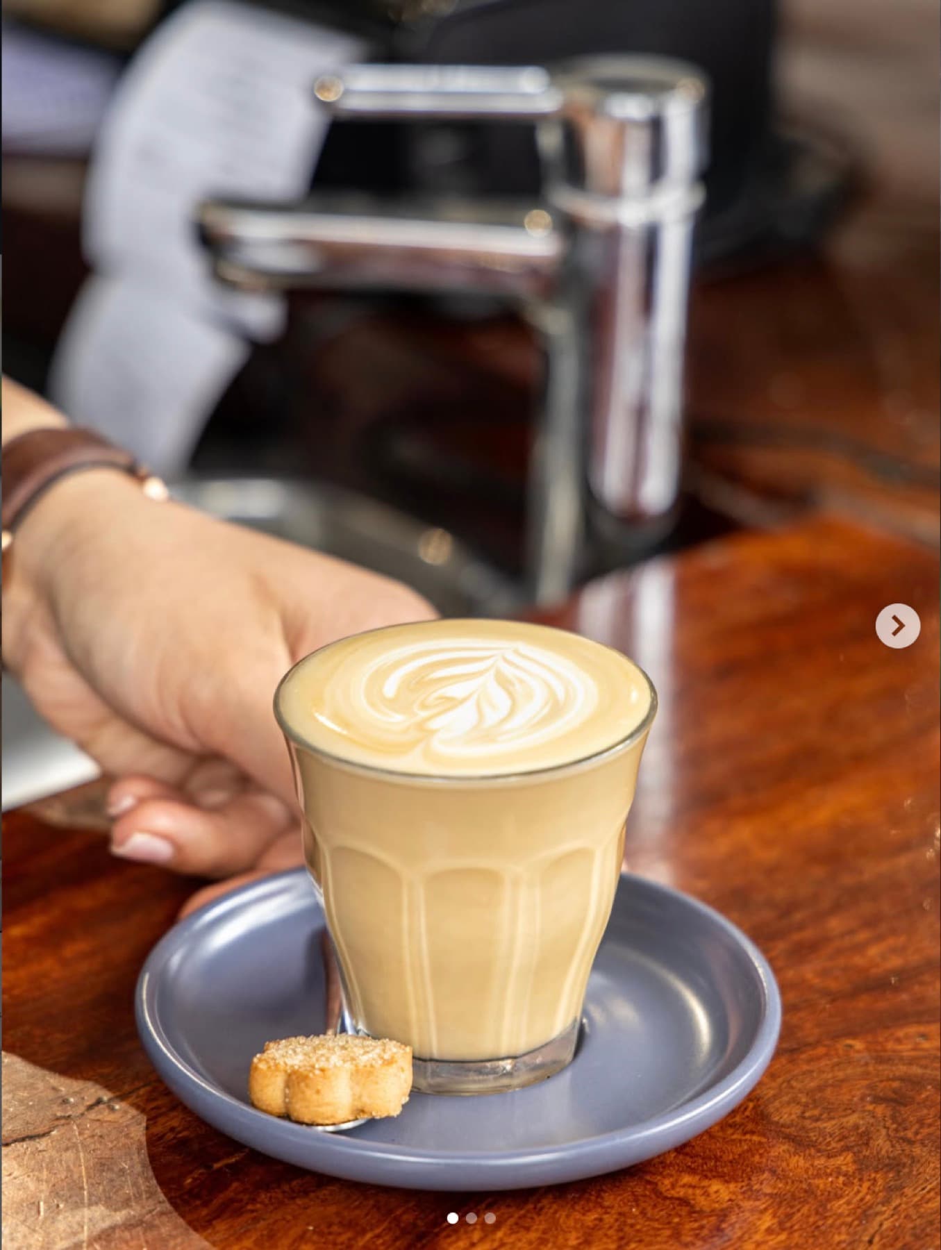 A flat white in a ribbed glass held beside the espresso machine