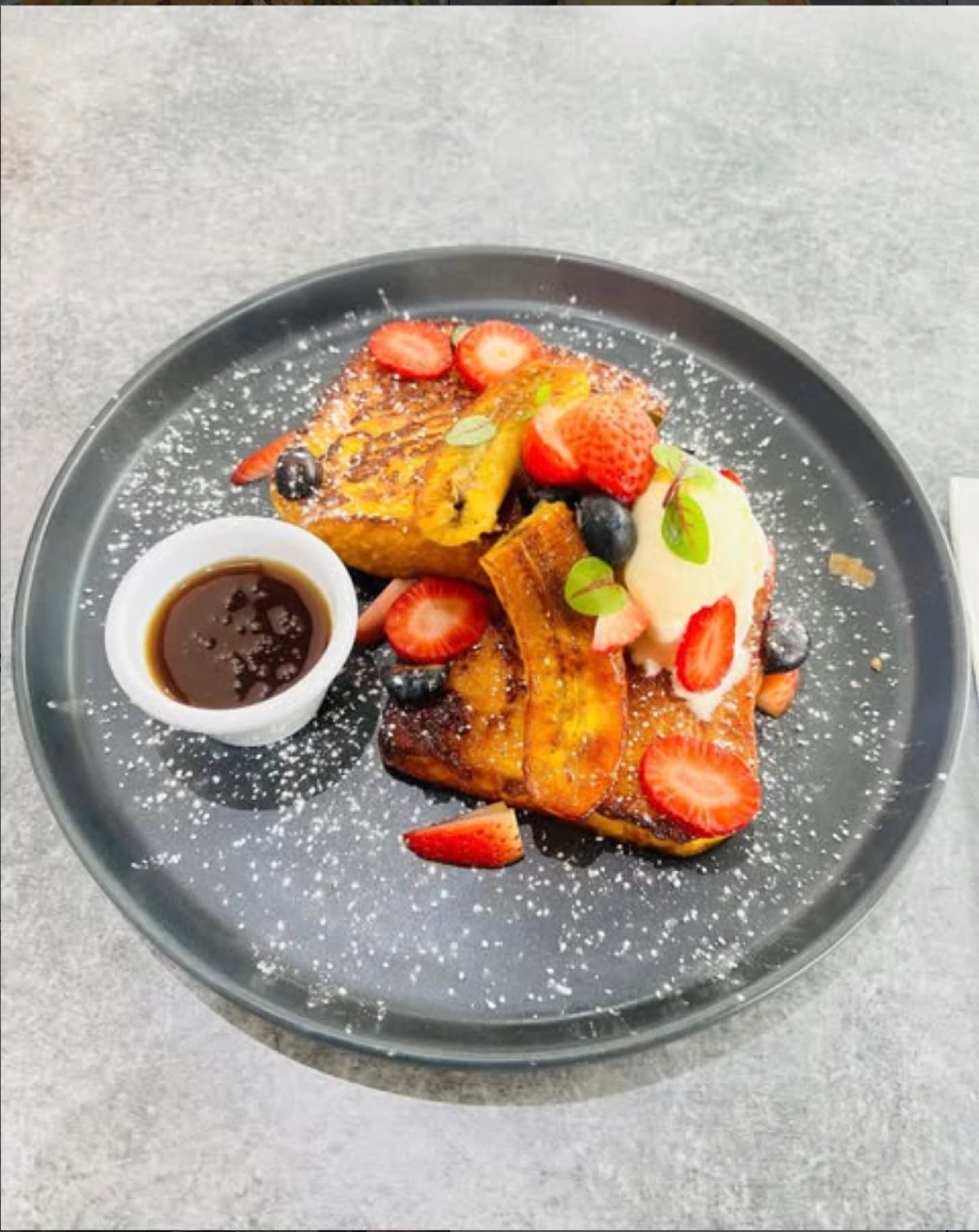 French toast dusted with icing sugar, with strawberries, blueberries, banana and maple syrup