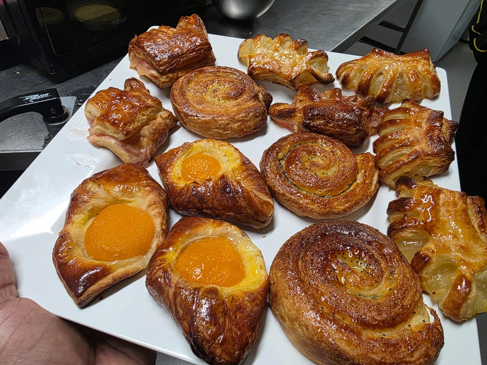 A plate of pastries — ham and cheese croissants, poppy seed scrolls, apricot danishes and turnovers