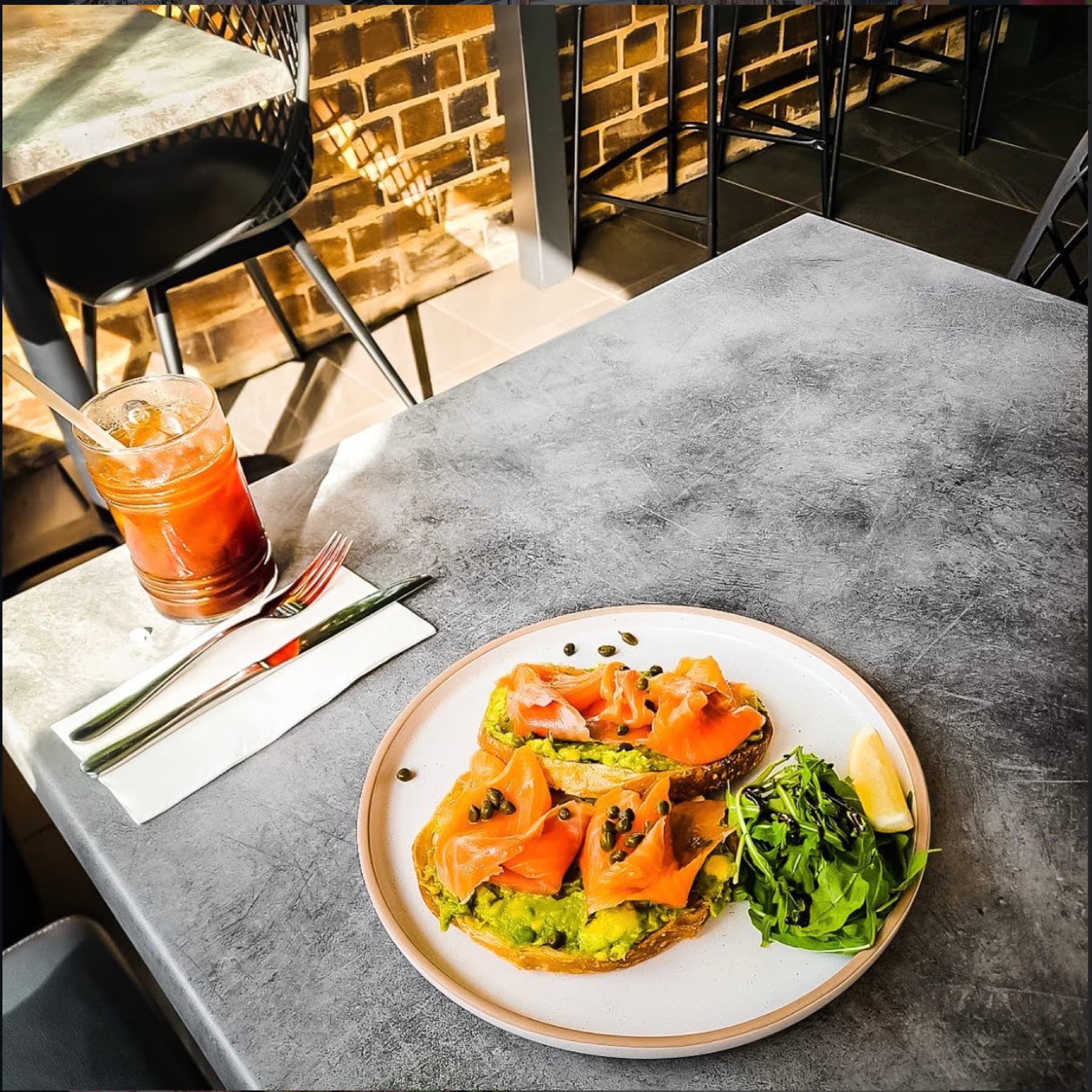 Smoked salmon and avocado on sourdough on a concrete table, brick wall and bar stools behind