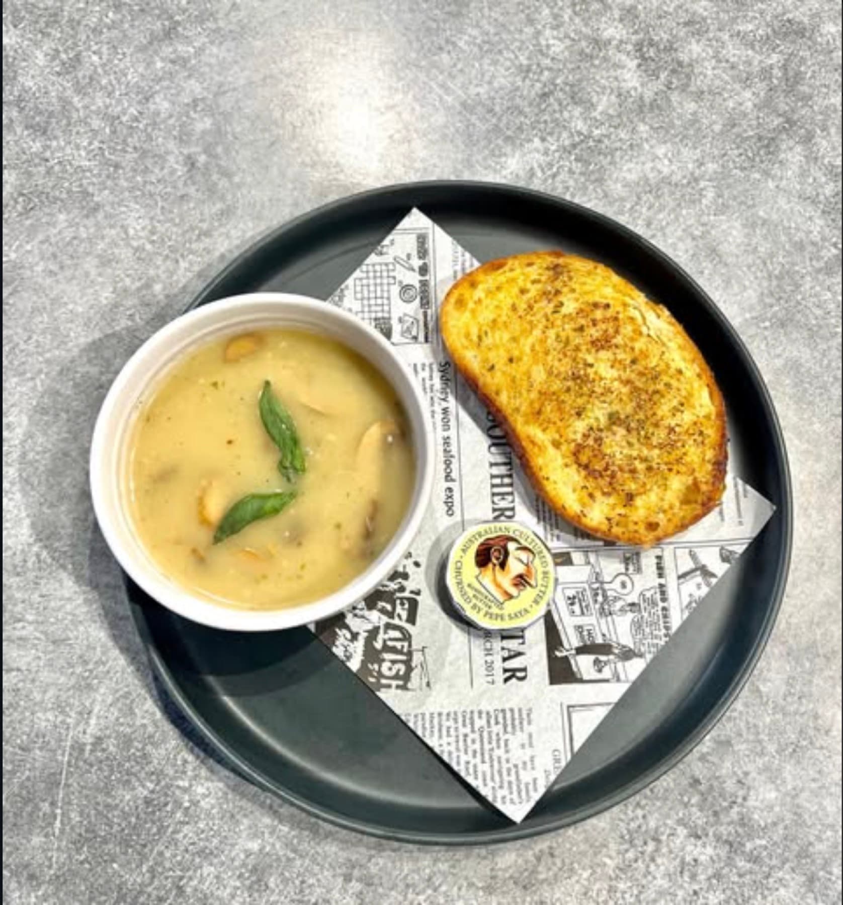 A cup of mushroom soup with basil, served with a thick slice of garlic bread
