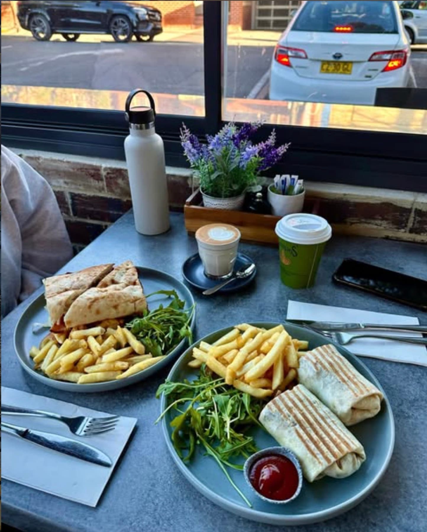 Two plates of wraps and chips with coffees on the window bar, Burlington Road outside