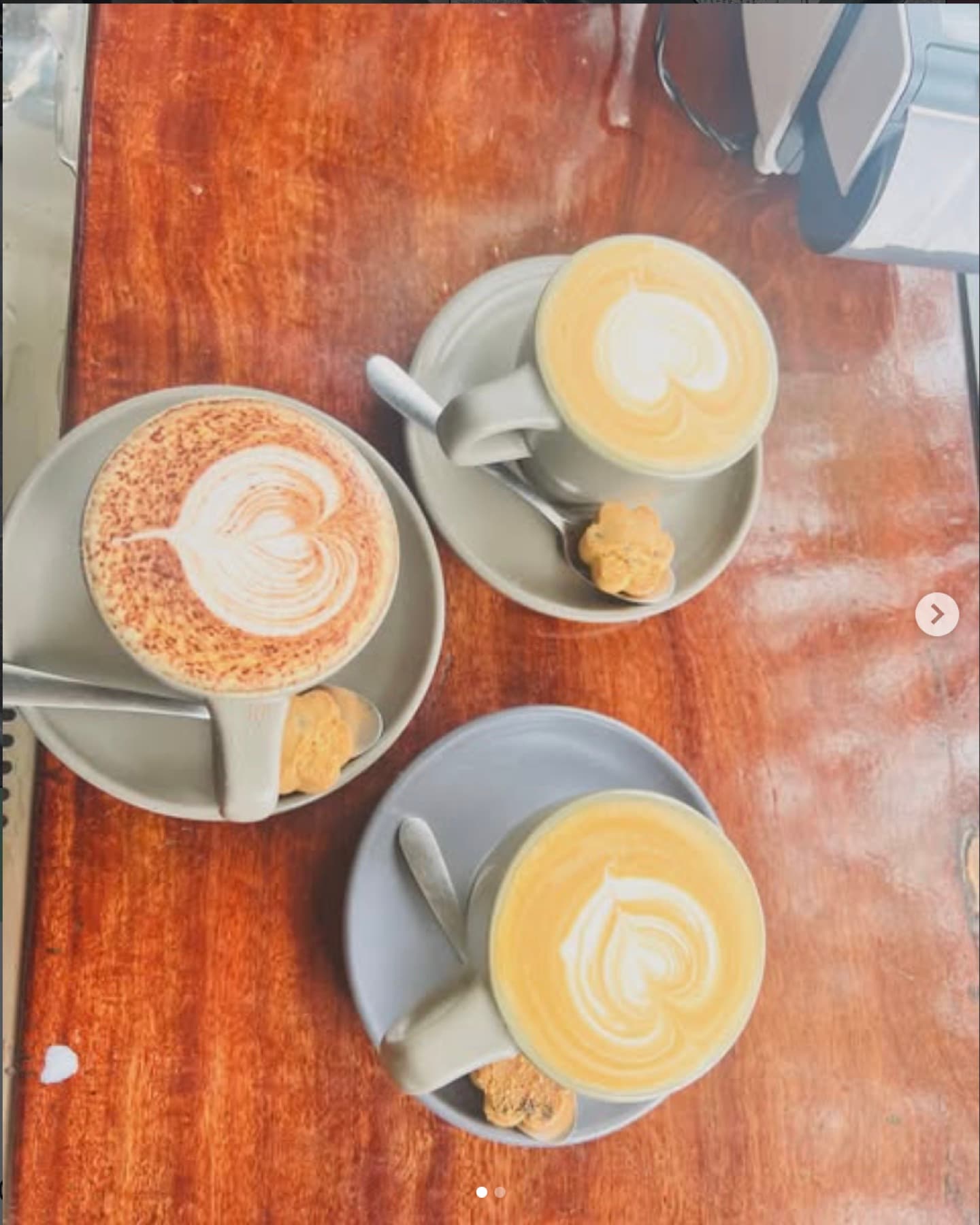 Three cappuccinos with heart latte art on a timber table, each with a shortbread biscuit