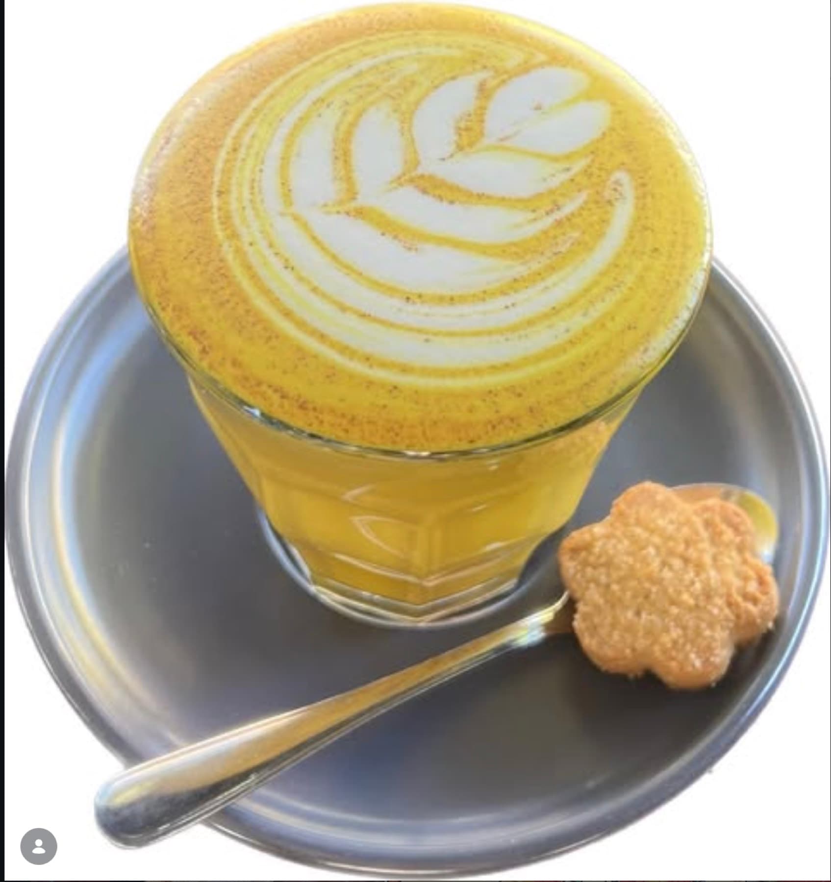 A turmeric latte with a tulip pattern, served on a metal saucer with a flower biscuit