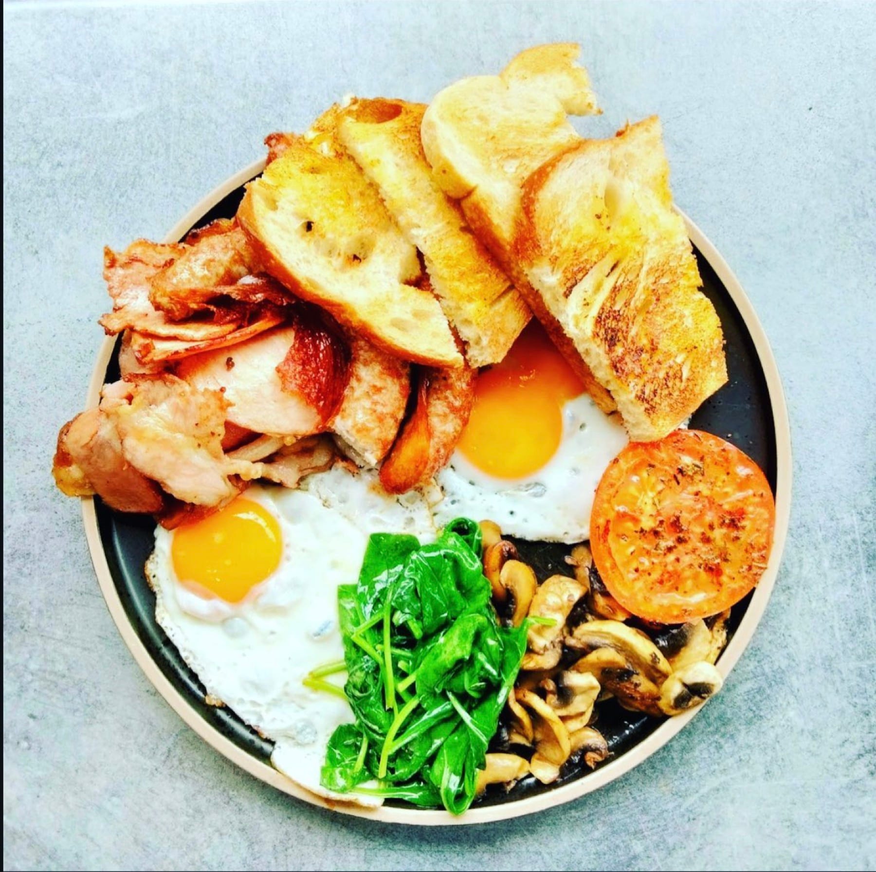 Big breakfast with fried eggs, bacon, mushrooms, wilted spinach, grilled tomato and toasted sourdough