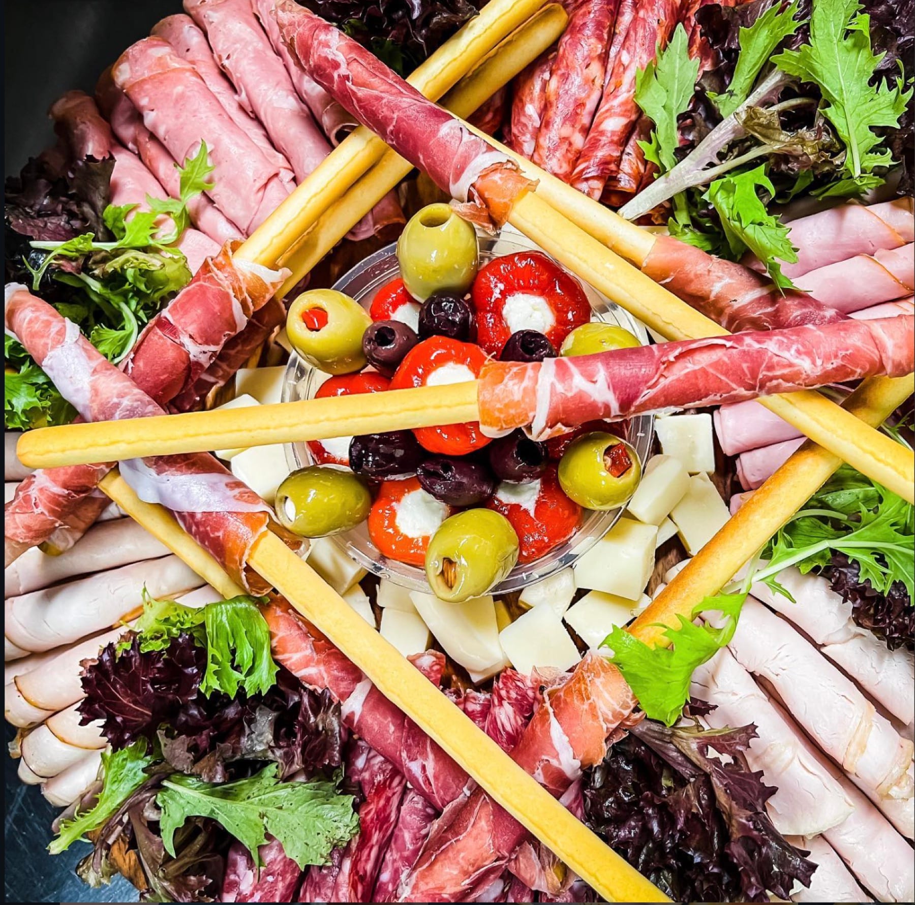 Close view of rolled prosciutto, salami, olives, cheese and grissini on a platter