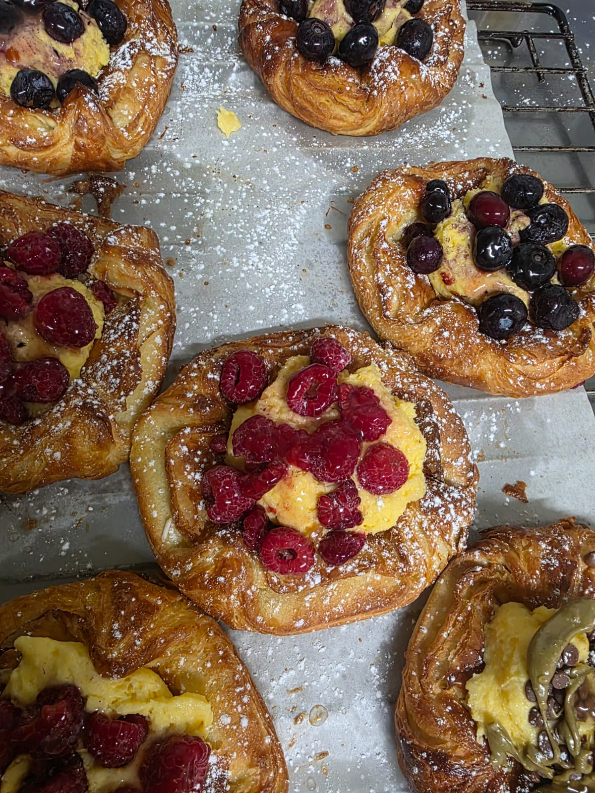 Berry danishes dusted with icing sugar, resting on baking paper beside a cooling rack