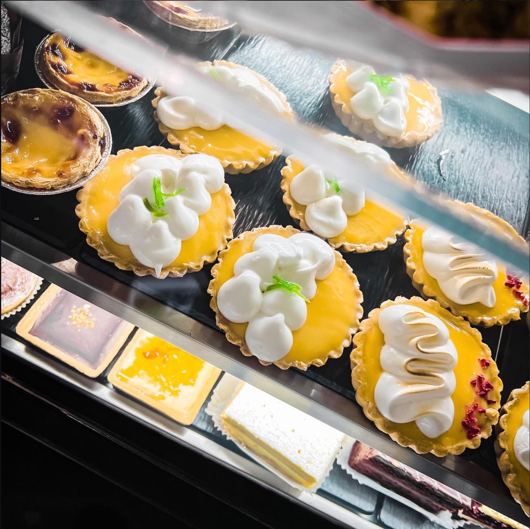 A tray of lemon meringue tarts and Portuguese custard tarts behind glass