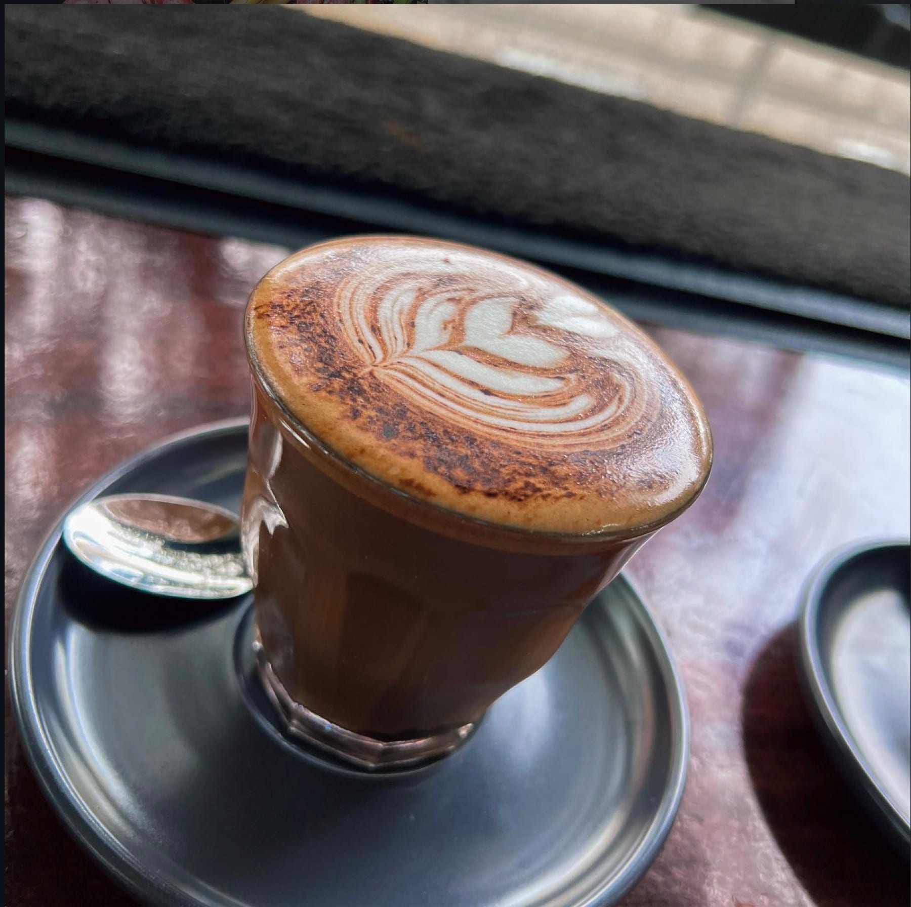 A piccolo latte in a small glass on a metal saucer by the window