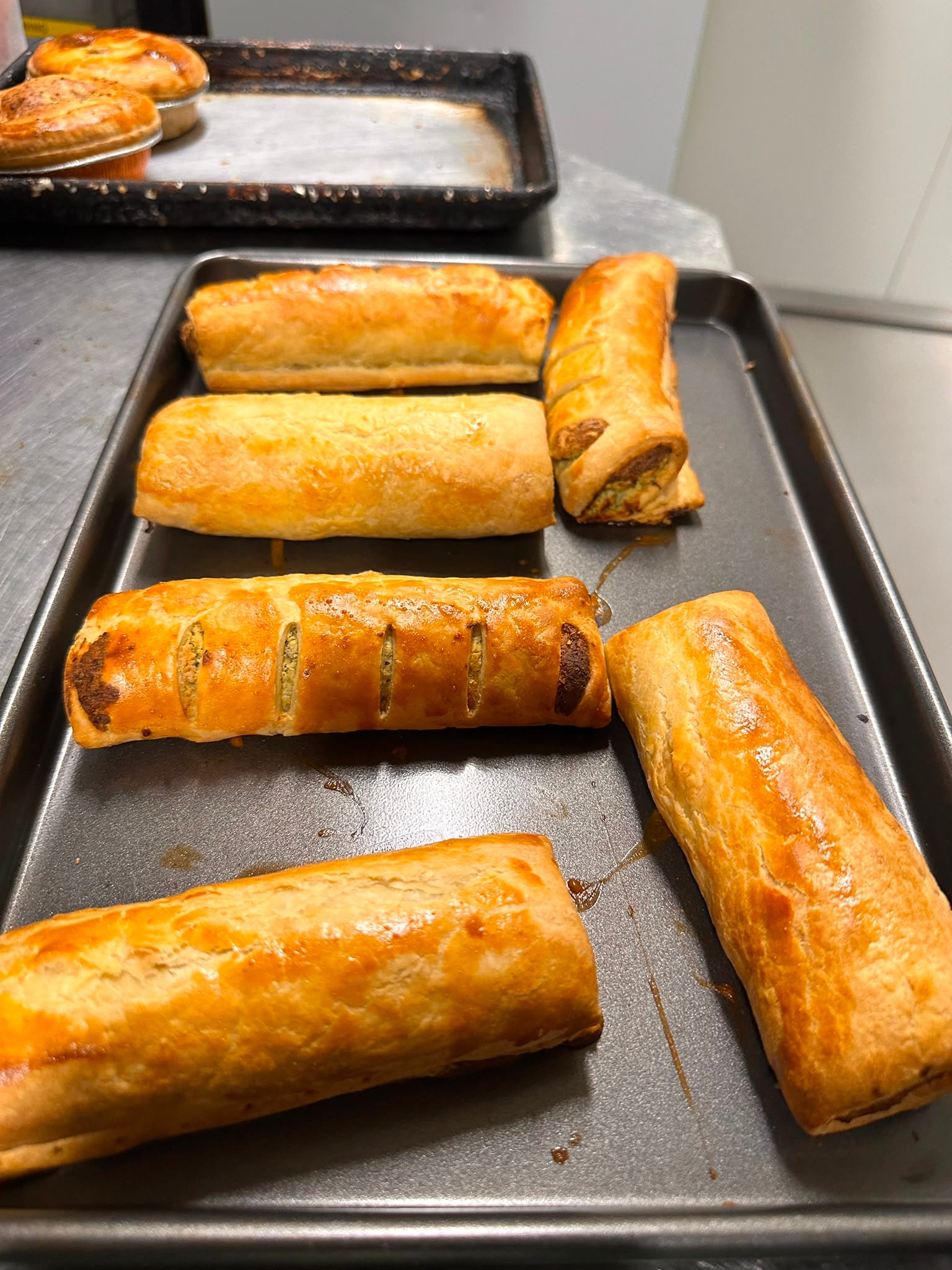 Sausage rolls and spinach rolls on a baking tray, pastry blistered and golden