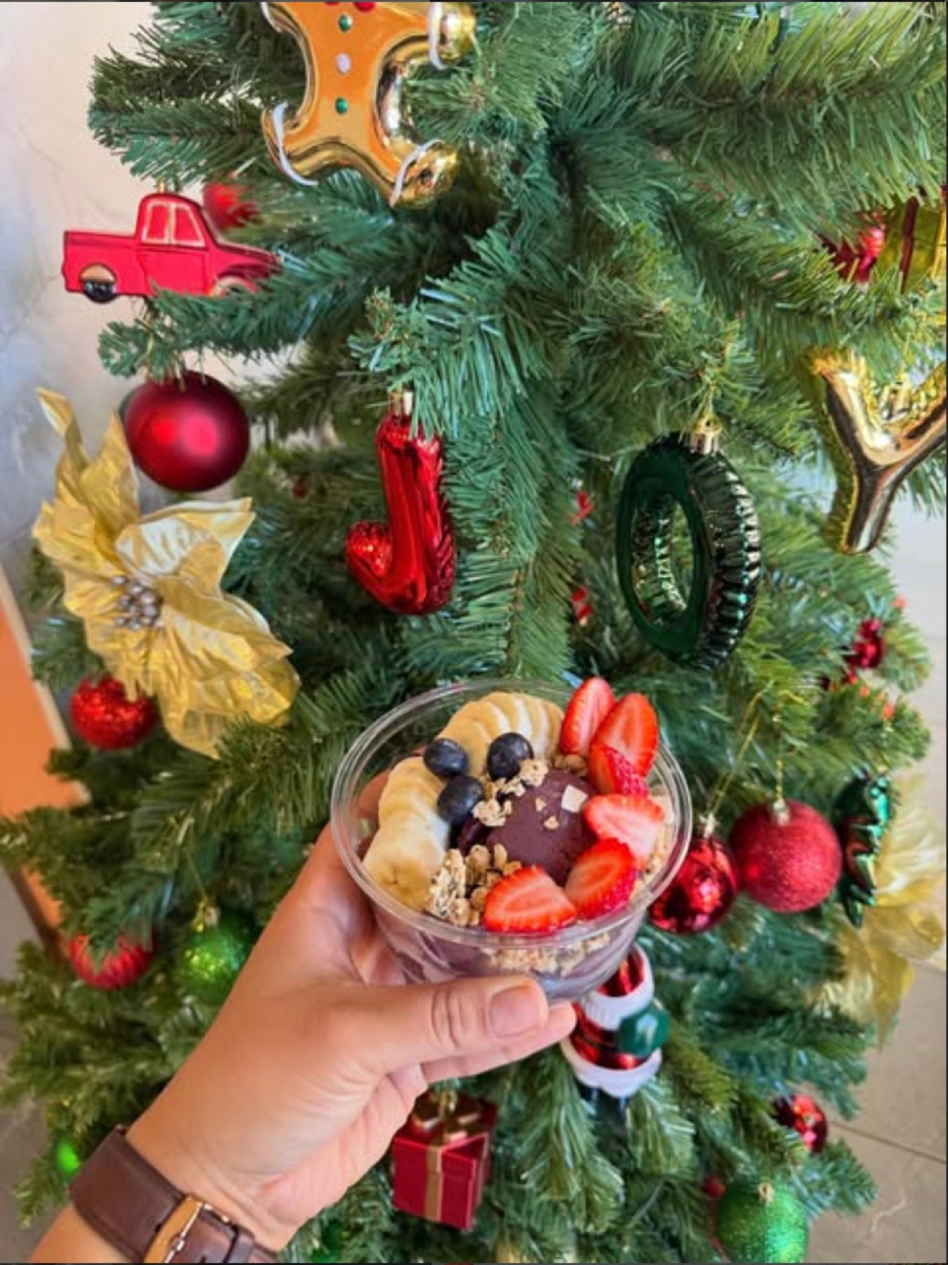 An açaí bowl held up in front of a decorated Christmas tree
