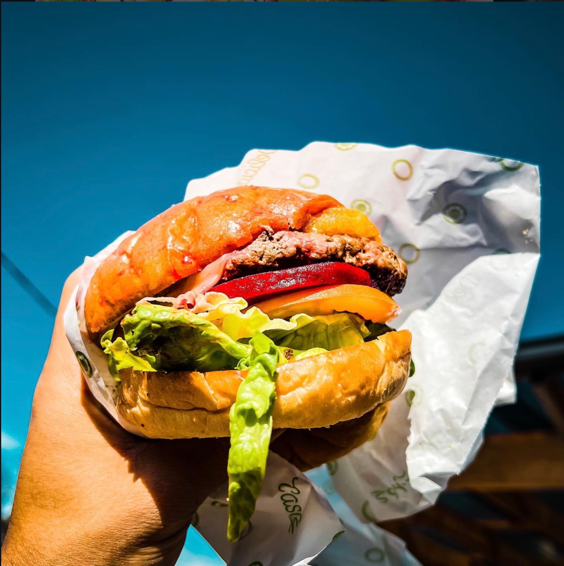 A beef burger in wrapping paper held up against a clear blue sky