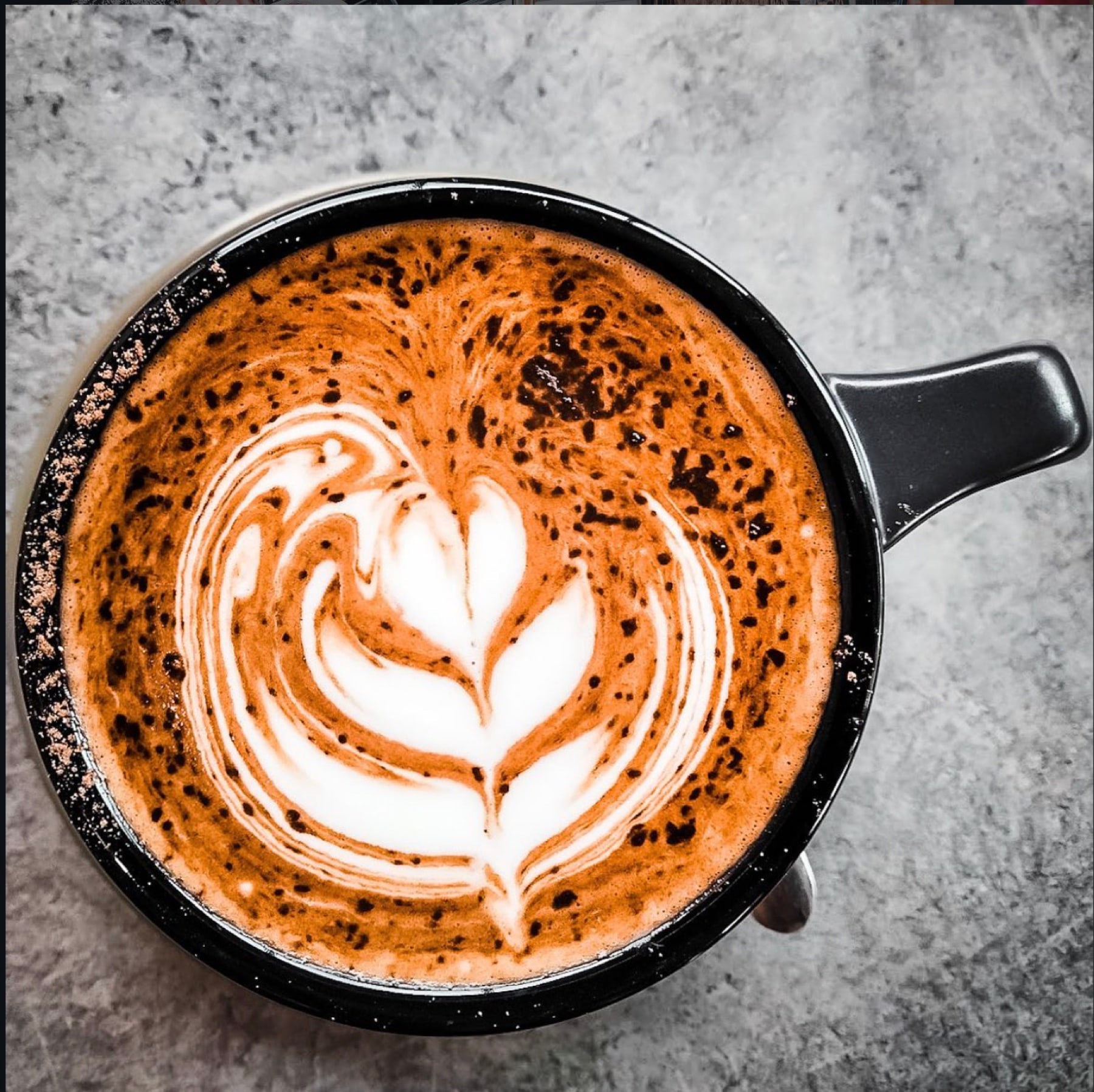 Overhead view of a rosetta poured into a black enamel mug on a concrete bench