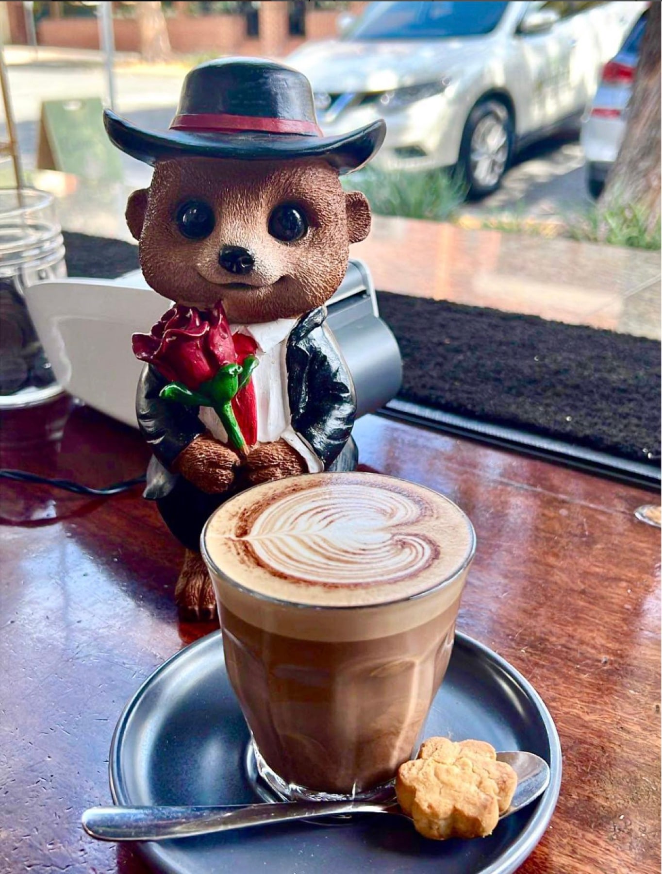 A latte on the window bar beside a small meerkat figurine in a top hat