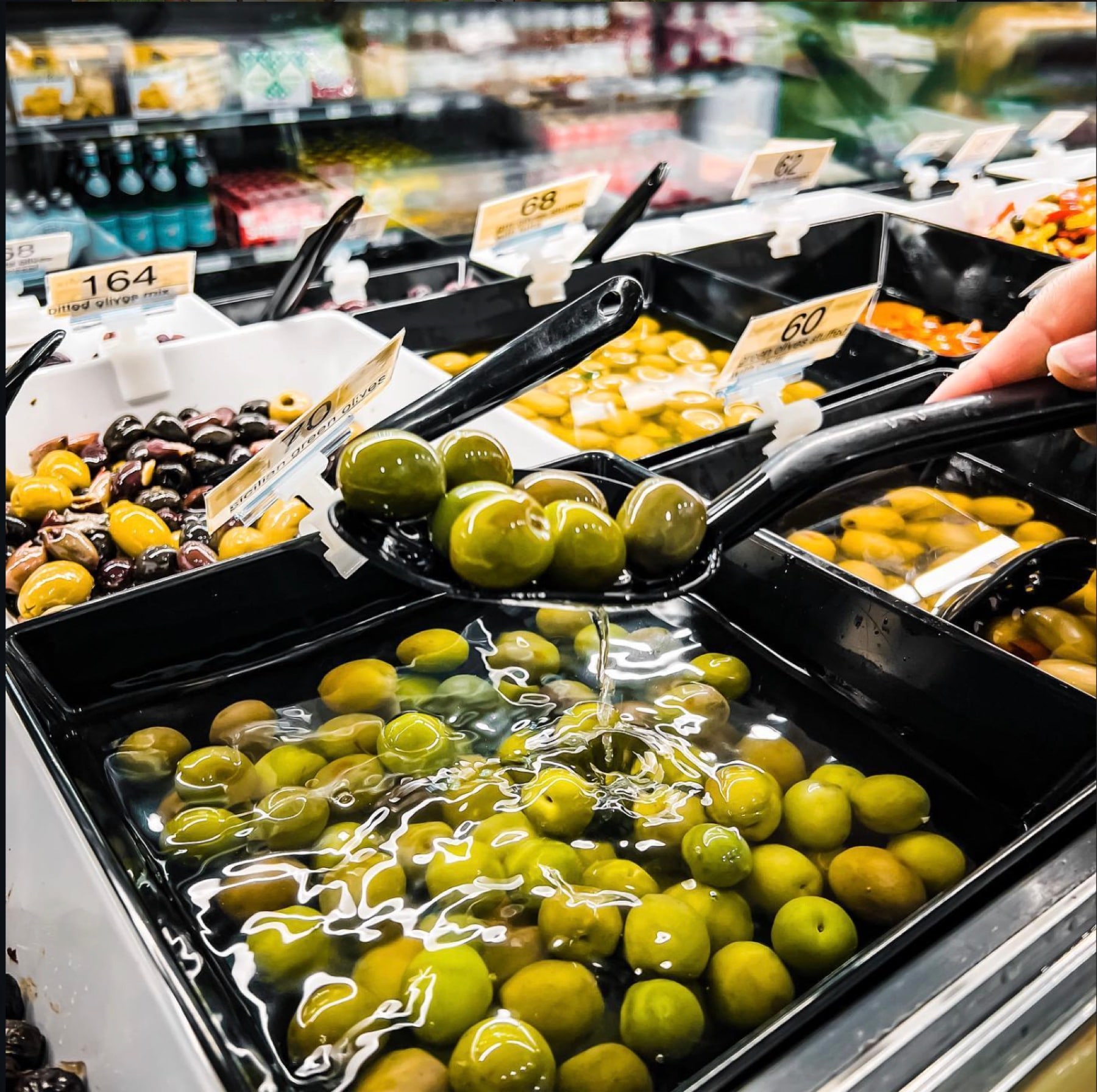 Trays of green, black and mixed olives in oil with serving tongs