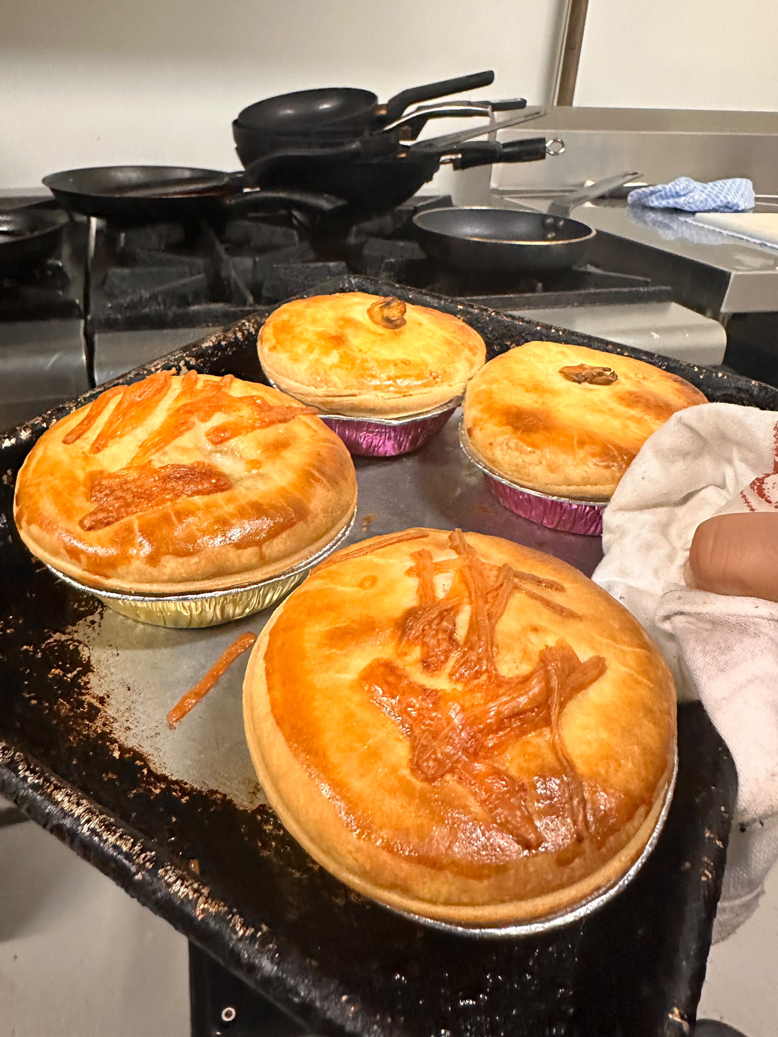 Pies cooling on a tray beside the stove, tops decorated with pastry offcuts