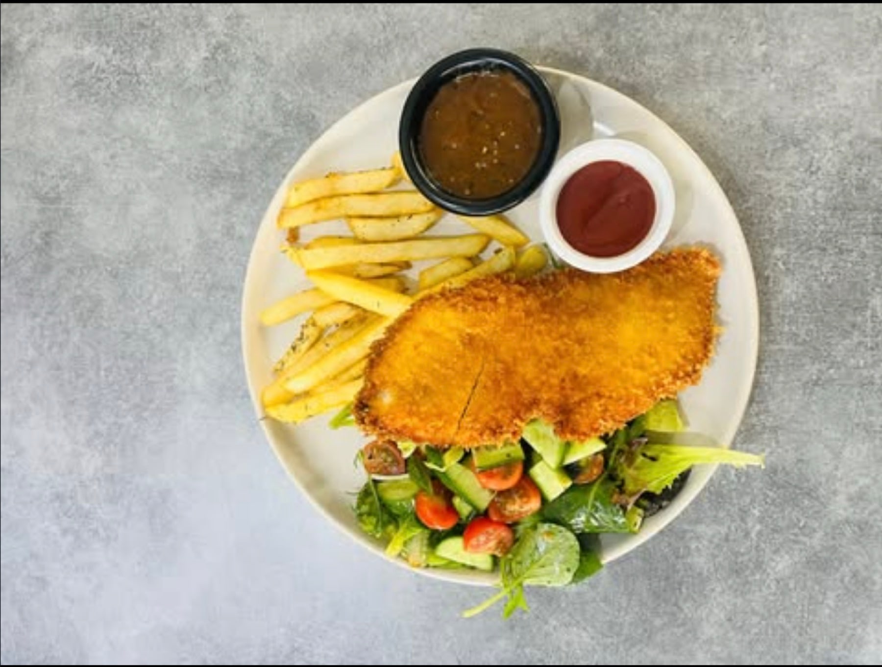 Chicken schnitzel with chips, garden salad and gravy, viewed from above