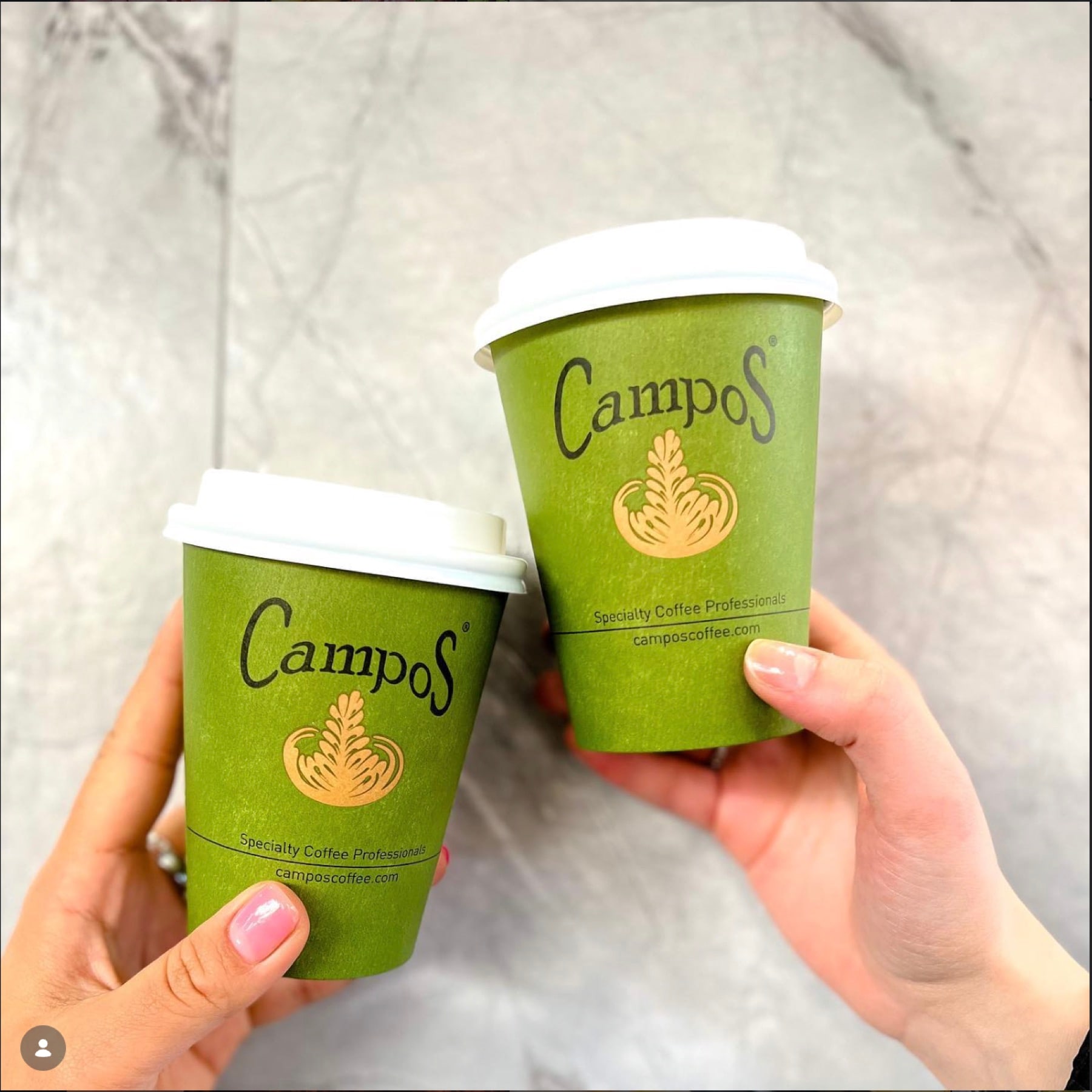Two takeaway coffee cups held up against a pale marble wall